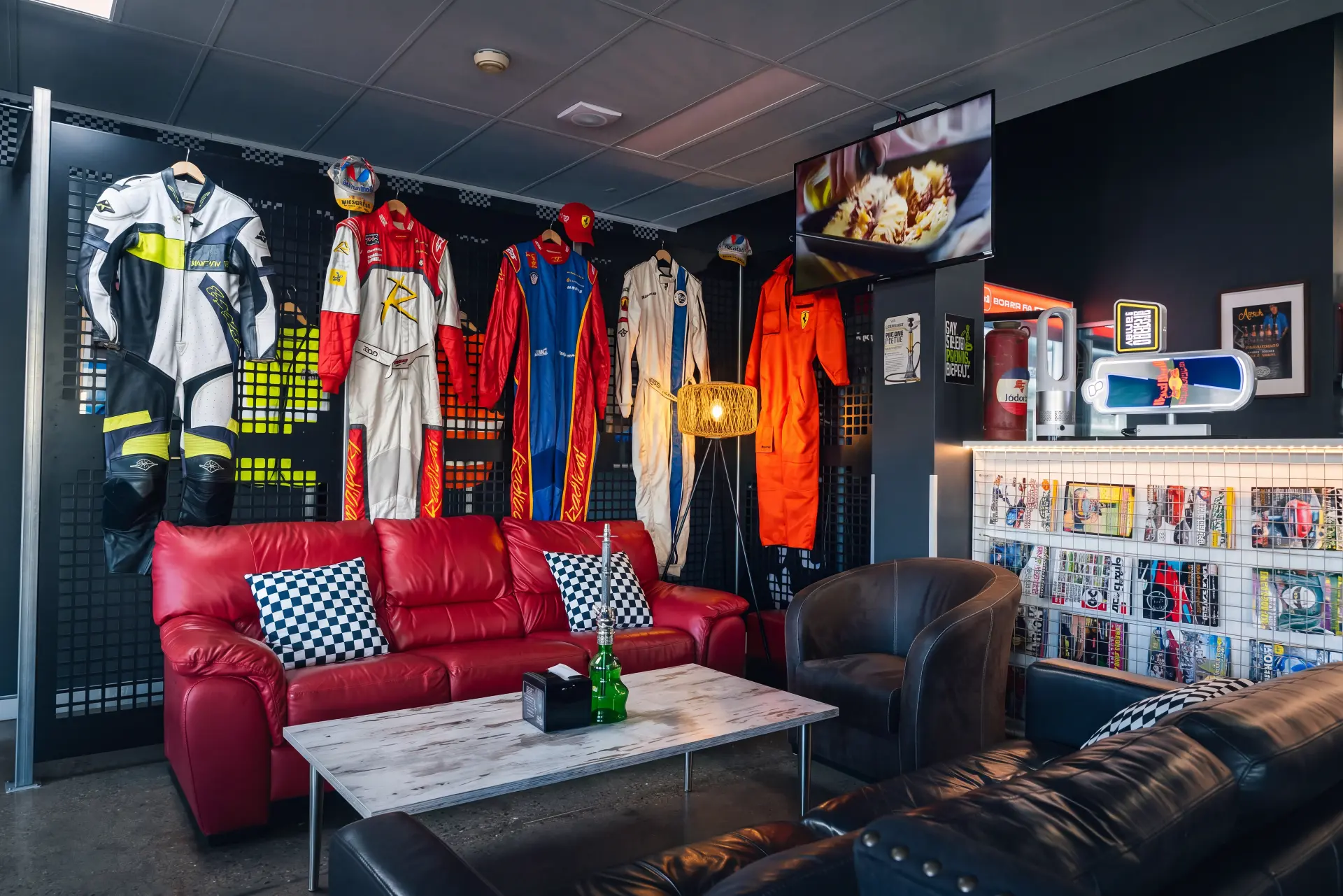 Red leather lounge and coffee table beneath the wall of racing suits and leathers
