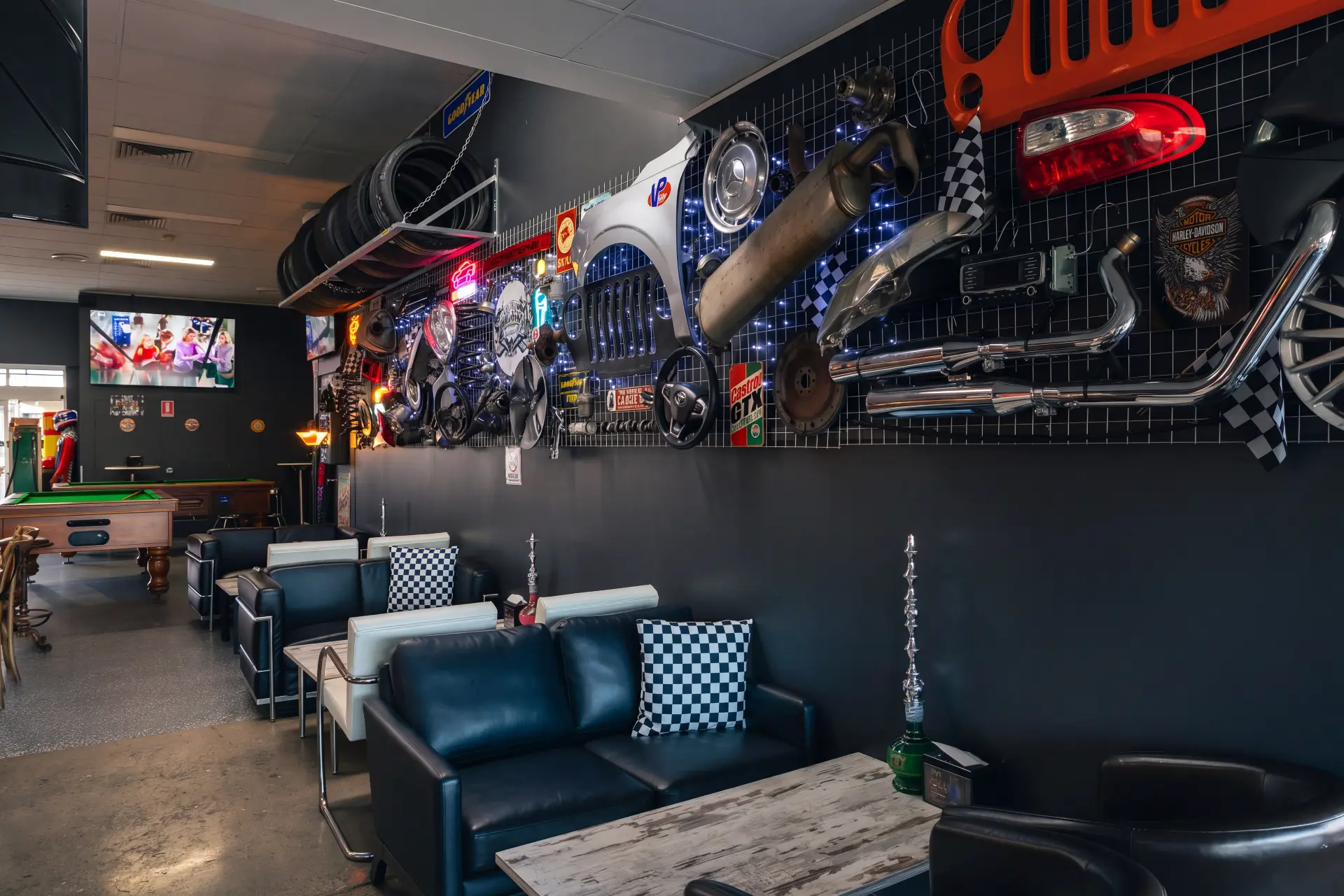 Dark leather lounges with checkered cushions along the wall of car parts, exhausts and screens